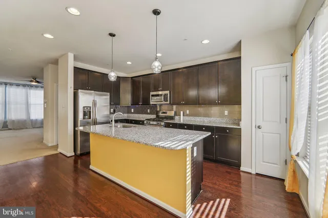 a kitchen with stainless steel appliances granite countertop a refrigerator a sink dishwasher a oven and a dining table with wooden floor