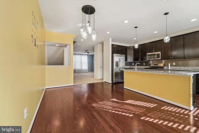 a kitchen with stainless steel appliances kitchen island granite countertop a refrigerator a stove and a sink with wooden floor