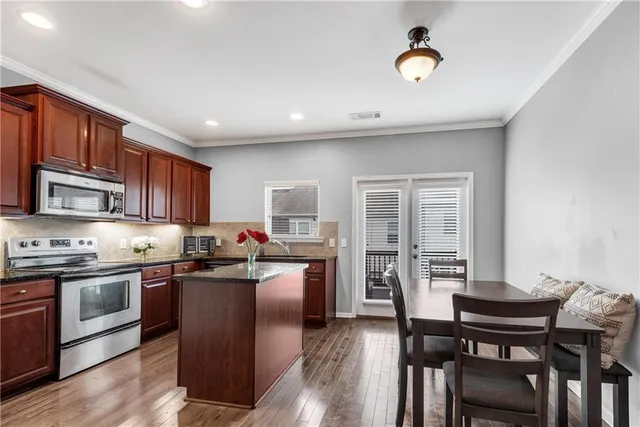 a kitchen with stainless steel appliances granite countertop a stove top oven a sink dishwasher a dining table and chairs with wooden floor