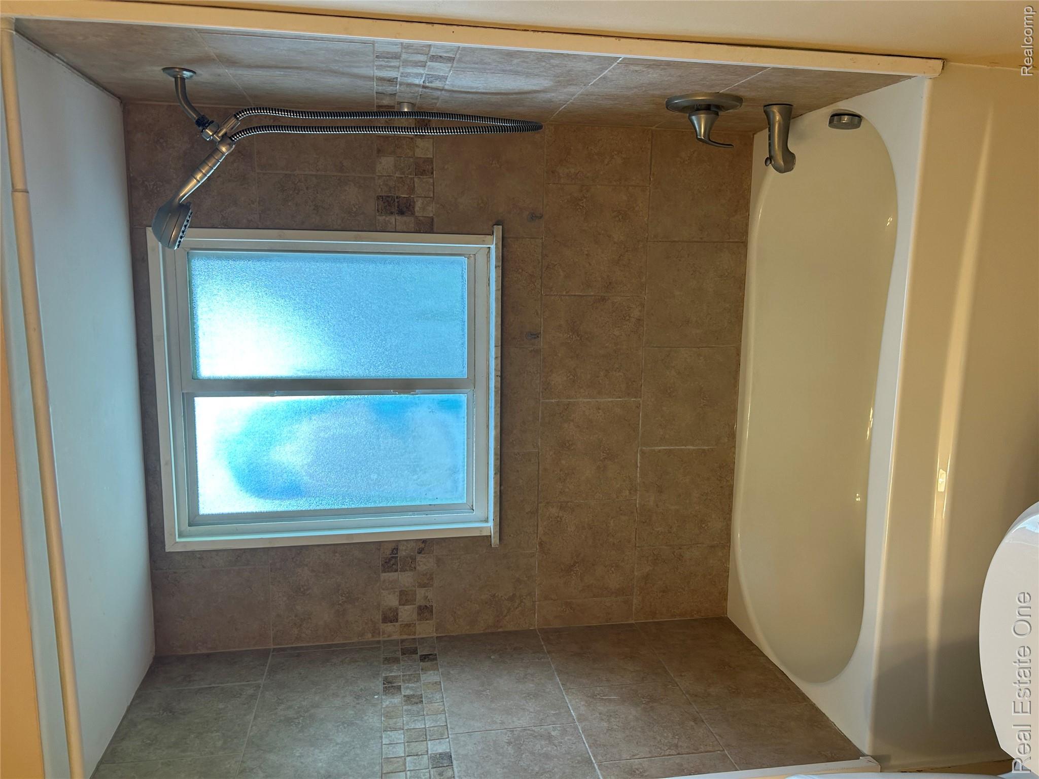 2659 Benstein Road Commerce Township, MI 48382 - Photo 18 of 26 Bathtub with tile surround featuring a decorative accent band, a double-paned frosted window, and a wall-mounted shower head with a handheld option