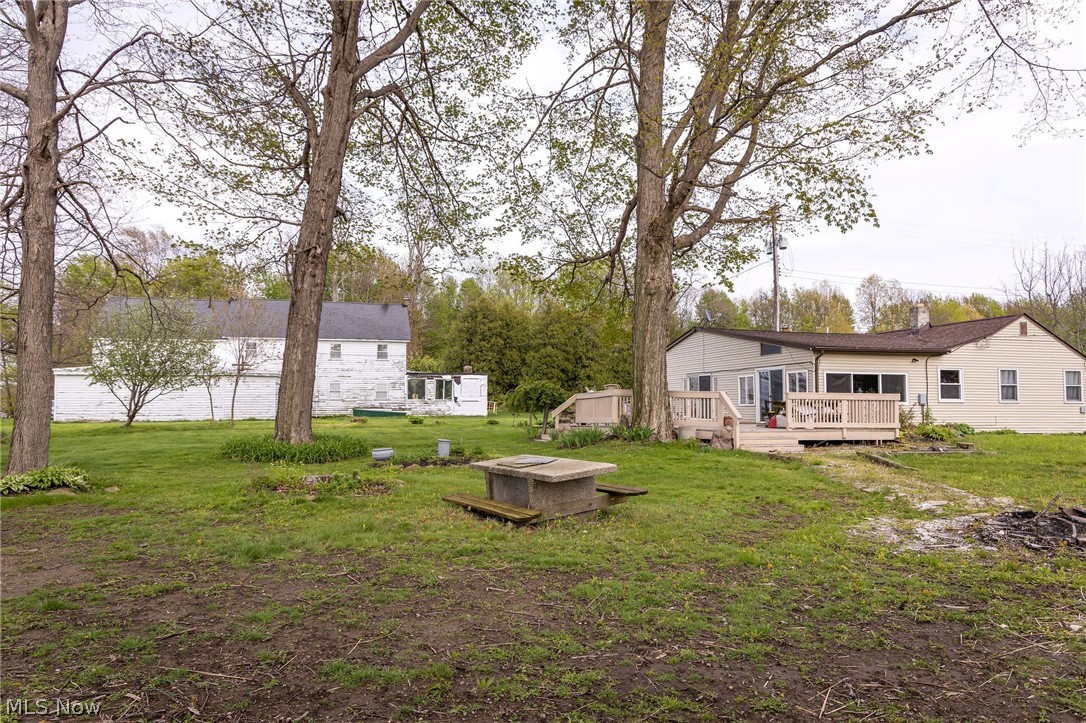 5467 Chapel Road Madison, OH 44057 - Photo 4 of 50 Expansive outdoor space featuring a beige ranch-style home with a multi-level wood deck, a white two-story outbuilding, mature trees, and a concrete picnic table