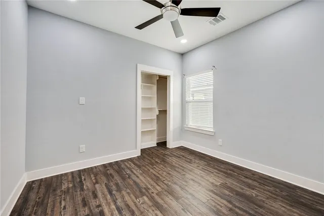 an empty room with wooden floor chandelier fan and windows