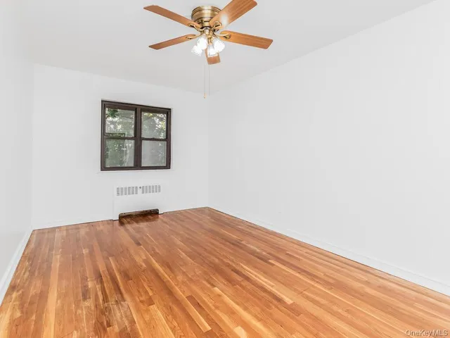 a view of an empty room with wooden floor and a fan