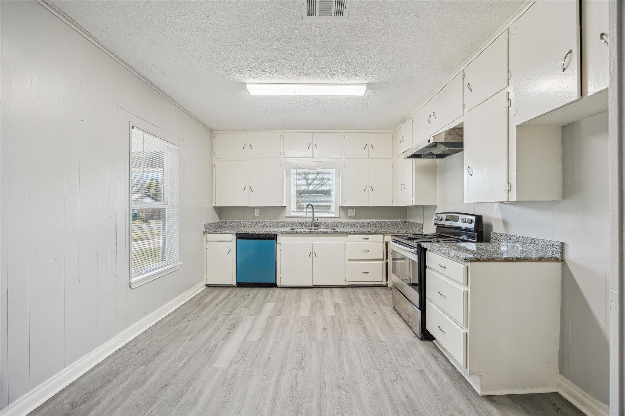 710 East Magnolia Street Angleton, TX 77515 - Photo 5 of 9 a kitchen with stainless steel appliances granite countertop a stove a sink dishwasher and white cabinets with wooden floor