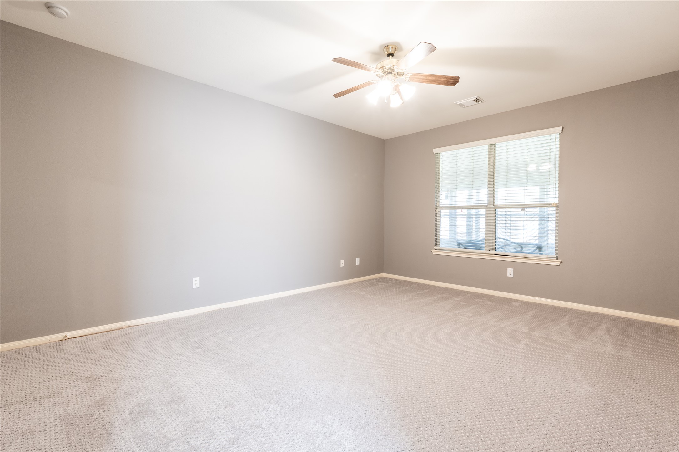 10619 Crownsedge Drive Spring, TX 77379 - Photo 21 of 38 This room features neutral gray walls and carpet, a ceiling fan with lights, and a large window with blinds, creating a bright and inviting space.