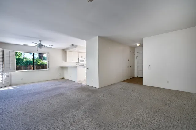 an empty room with windows and way to kitchen