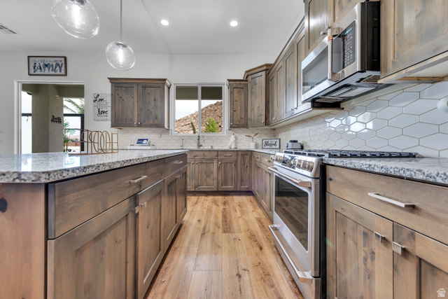 6105 Bunda Way St. George, UT 84790 - Photo 14 of 49 Kitchen featuring wood-finish cabinetry, granite-style countertops, stainless steel appliances, a white geometric tile backsplash, and wood-finish flooring