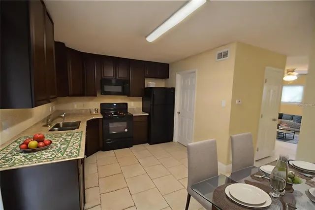 a kitchen with stainless steel appliances a refrigerator a sink a stove a dining table and chairs with wooden floor