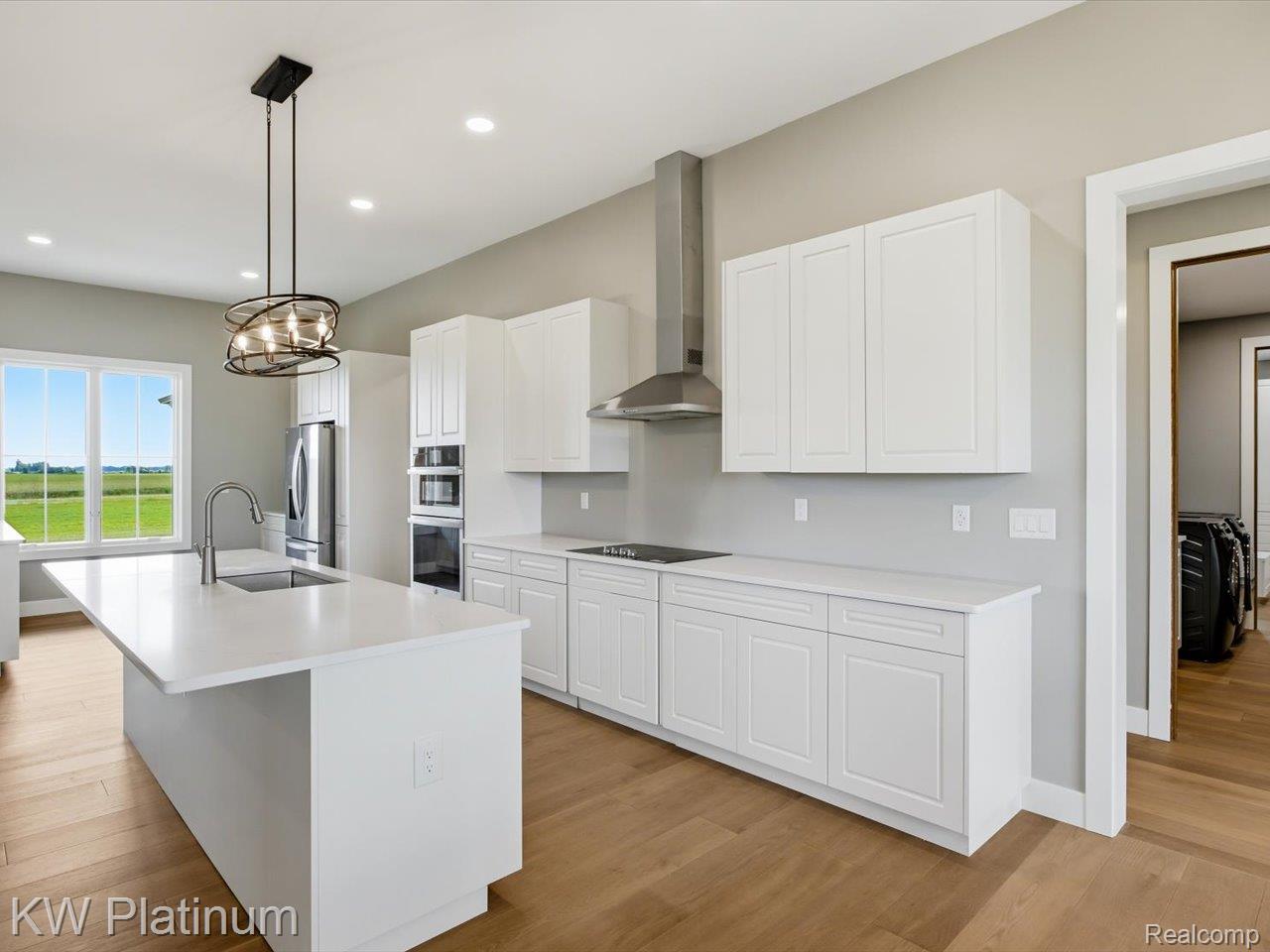 493 Wood Road Snover, MI 48472 - Photo 21 of 60 Modern kitchen featuring a large central island with an undermount sink, stainless steel appliances, white shaker cabinetry, and wood-finish flooring