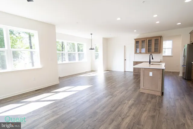 a large white kitchen with stainless steel appliances granite countertop a stove top oven a sink a refrigerator and white cabinets with wooden floor