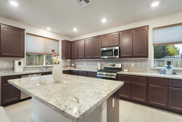 a kitchen with stainless steel appliances granite countertop a sink dishwasher a stove top oven a refrigerator with grey cabinets and wooden floor