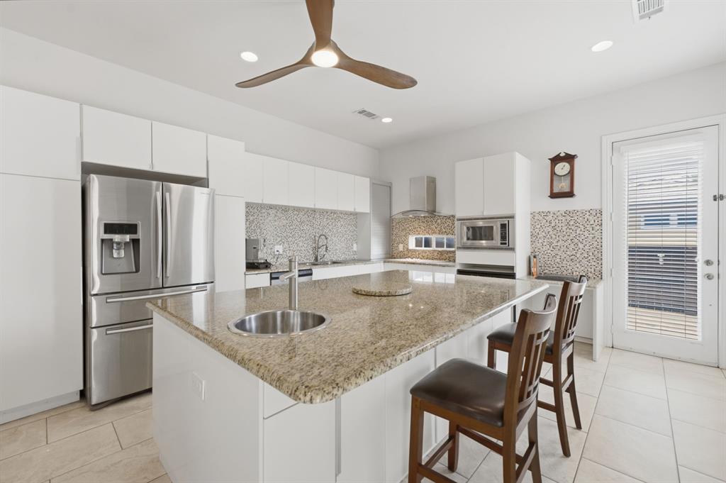 3315 Ricci Lane Irving, TX 75062 - Photo 15 of 40 Spacious kitchen featuring an expansive granite-top island with an integrated sink, stainless steel appliances, white cabinetry, and a mosaic tile backsplash