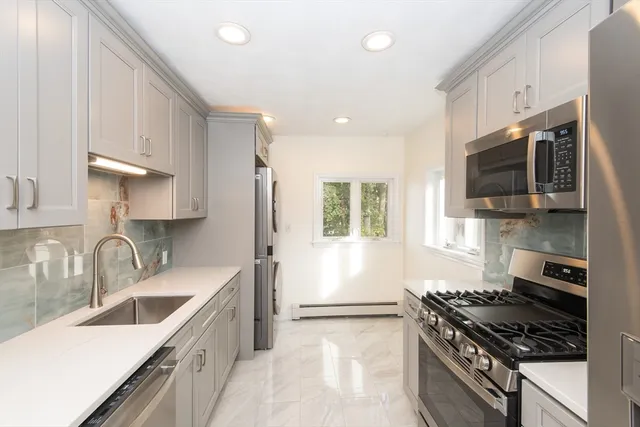 a kitchen with stainless steel appliances a sink a stove a microwave a refrigerator a sink and wooden cabinets