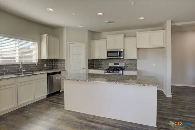 a kitchen with stainless steel appliances granite countertop a sink a stove a refrigerator a center island and cabinets