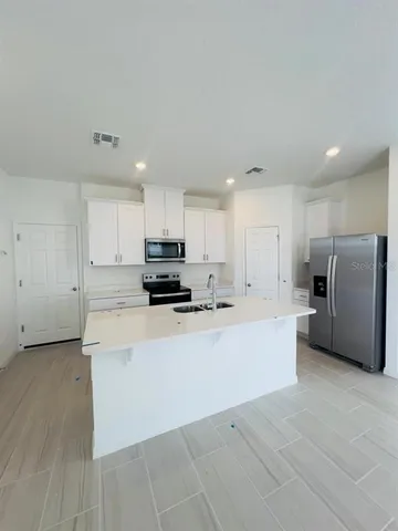 a large kitchen with stainless steel appliances a refrigerator a stove top oven a sink and cabinets