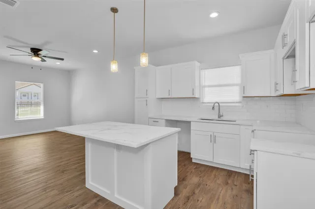 a kitchen with kitchen island a sink dishwasher a stove a refrigerator and white cabinets with wooden floor