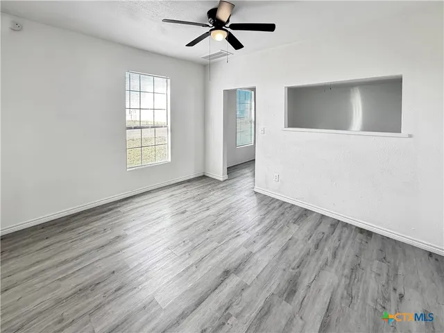 an empty room with wooden floor a ceiling fan and windows