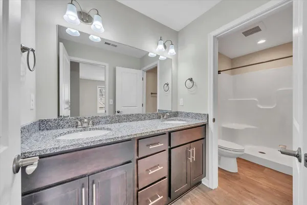a bathroom with a granite countertop double vanity sink toilet and shower