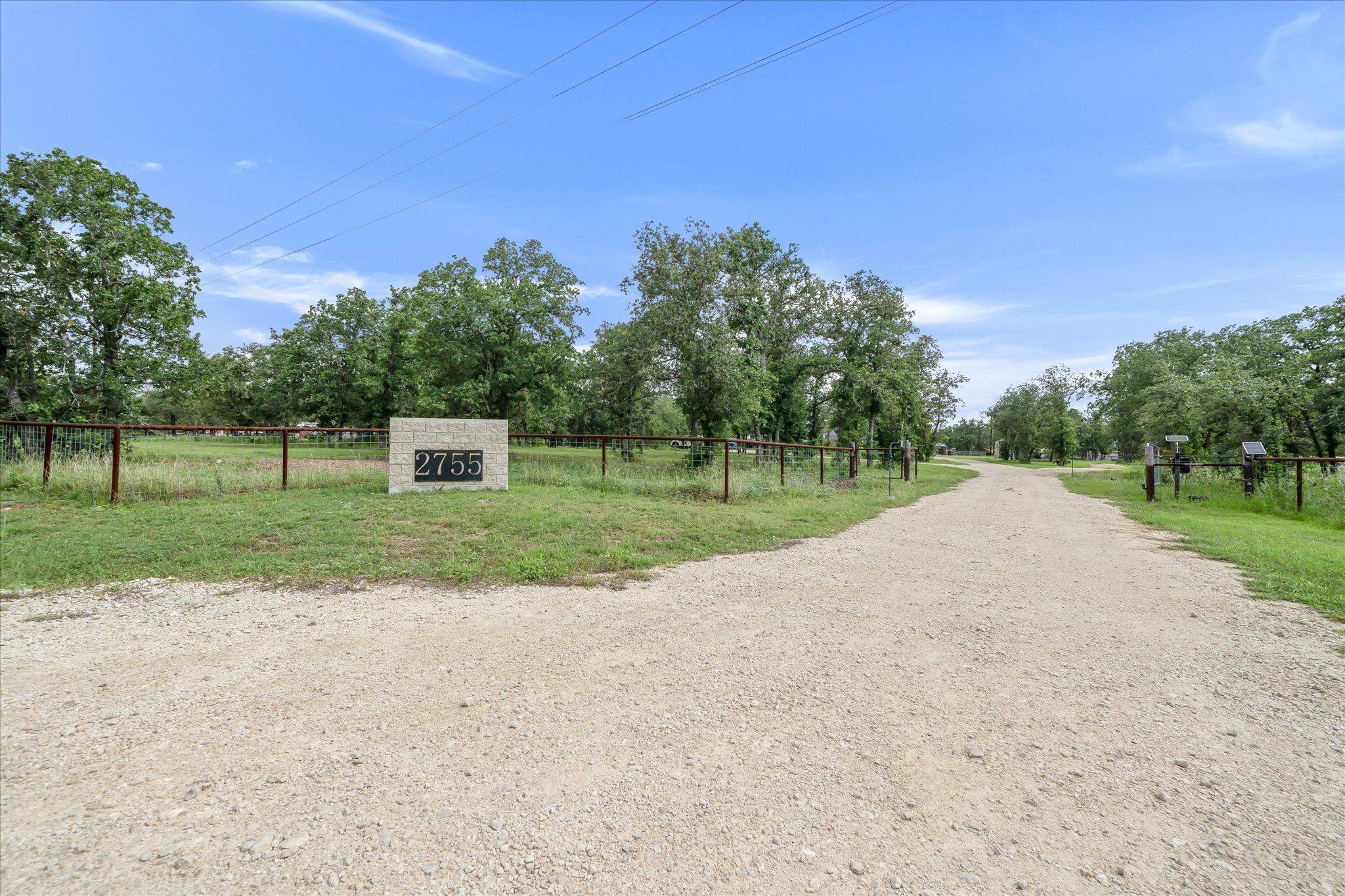 2755 Washburn Road Luling, TX 78648 - Photo 4 of 40 A long gravel driveway with a gated entry leads to this fenced rural property, offering seclusion and abundant natural beauty.