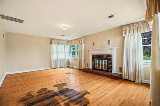 an empty room with wooden floor fireplace and windows