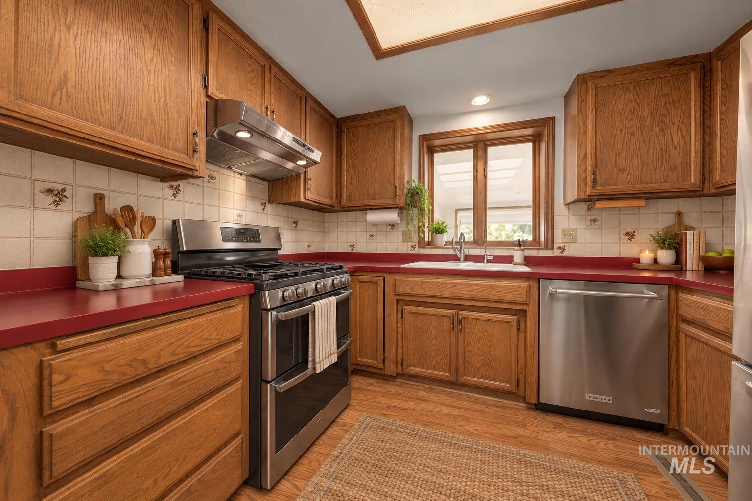 340 Pioneer Road Weiser, ID 83672 - Photo 18 of 44 Wood-finish flooring with oak cabinetry, red countertops, white tile backsplash, and stainless steel appliances