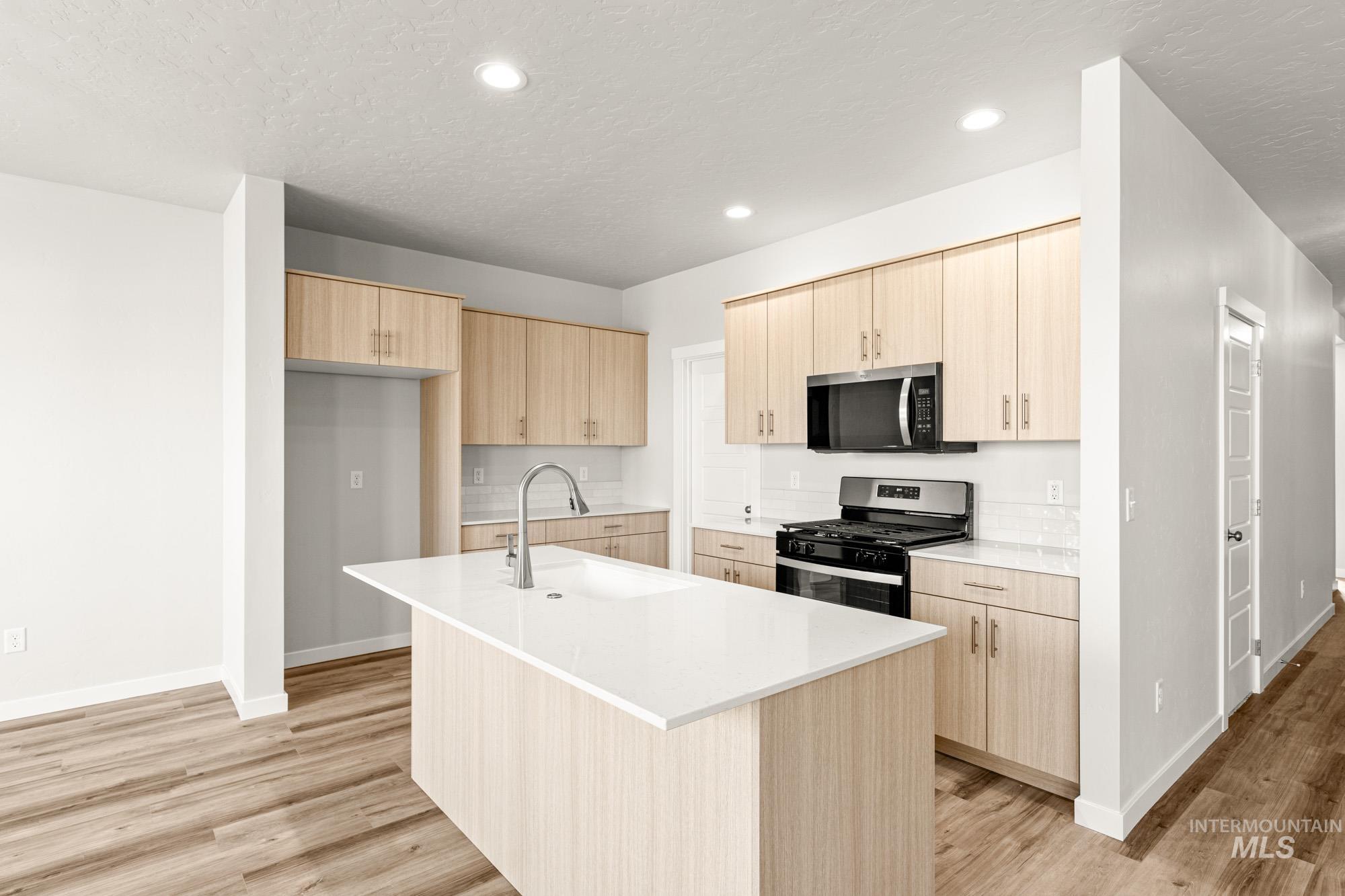 12865 Decatur Street Nampa, ID 83651 - Photo 4 of 20 Contemporary kitchen featuring wood-finish cabinetry, a central island with a built-in sink, white countertops, a tiled backsplash, and stainless steel appliances