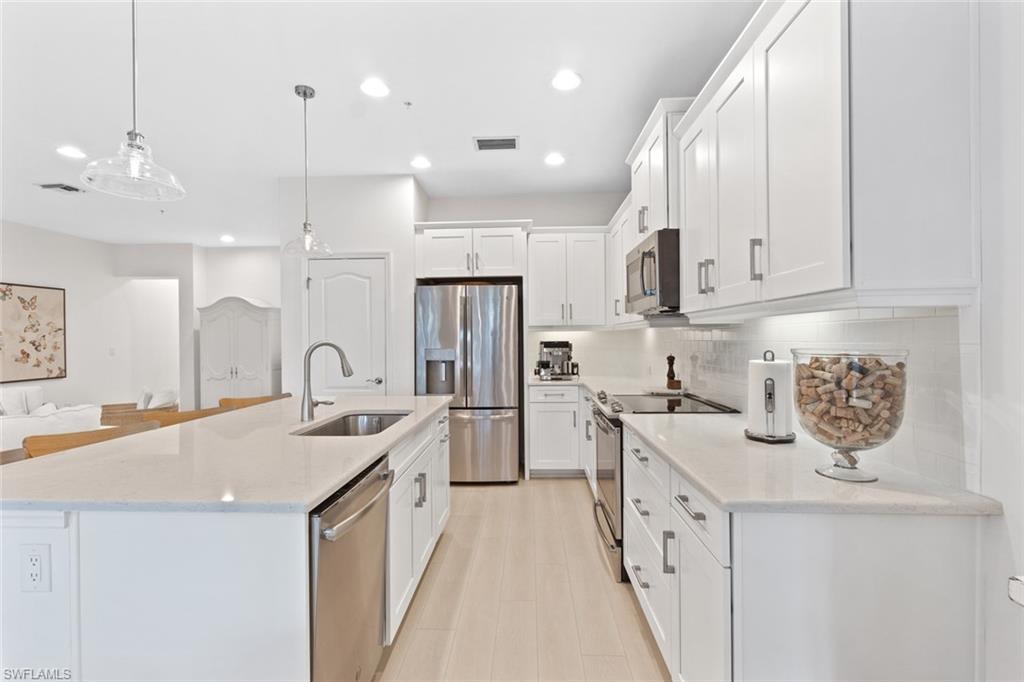 6973 Avalon Circle, Unit 1406 Naples, FL 34112 - Photo 6 of 36 Kitchen featuring stainless steel appliances, hanging light fixtures, white cabinetry, light stone counters, and an island with sink