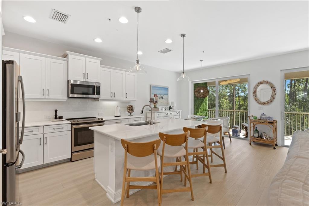 6973 Avalon Circle, Unit 1406 Naples, FL 34112 - Photo 7 of 36 Kitchen with stainless steel appliances, a kitchen bar, pendant lighting, white cabinetry, and an island with sink