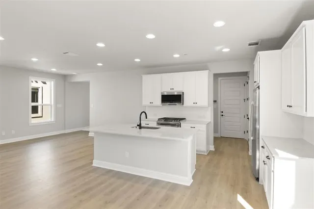 a large white kitchen with kitchen island a stove a sink a refrigerator and white cabinets with wooden floor