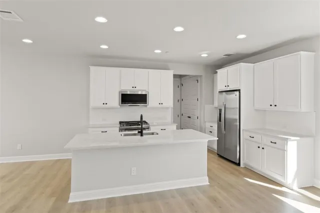 a kitchen with stainless steel appliances a sink a stove a refrigerator cabinets and wooden floor