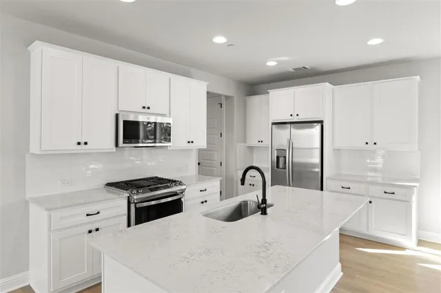 a large kitchen with stainless steel appliances a large counter top a stove a chimney a sink and white cabinets