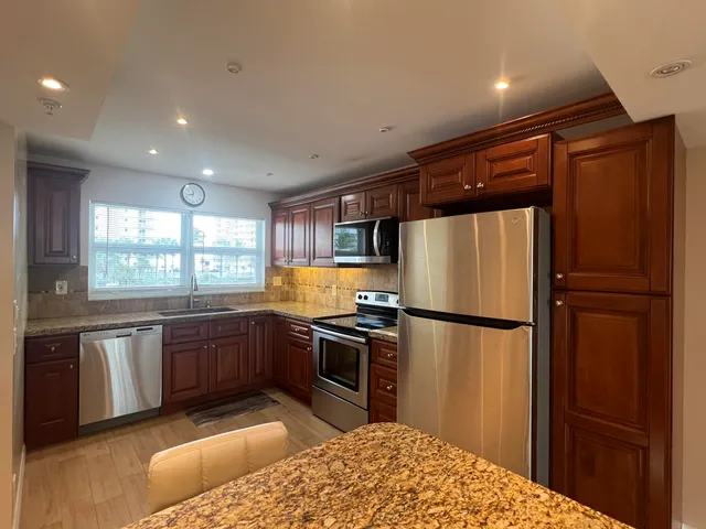 a kitchen with stainless steel appliances granite countertop a refrigerator a sink dishwasher a stove with white cabinets and wooden floor