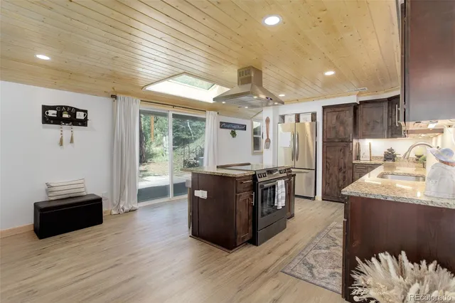 a kitchen with stainless steel appliances granite countertop a refrigerator a sink dishwasher a stove and a dining table with wooden floor