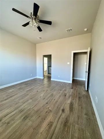 an empty room with wooden floor ceiling fan and windows