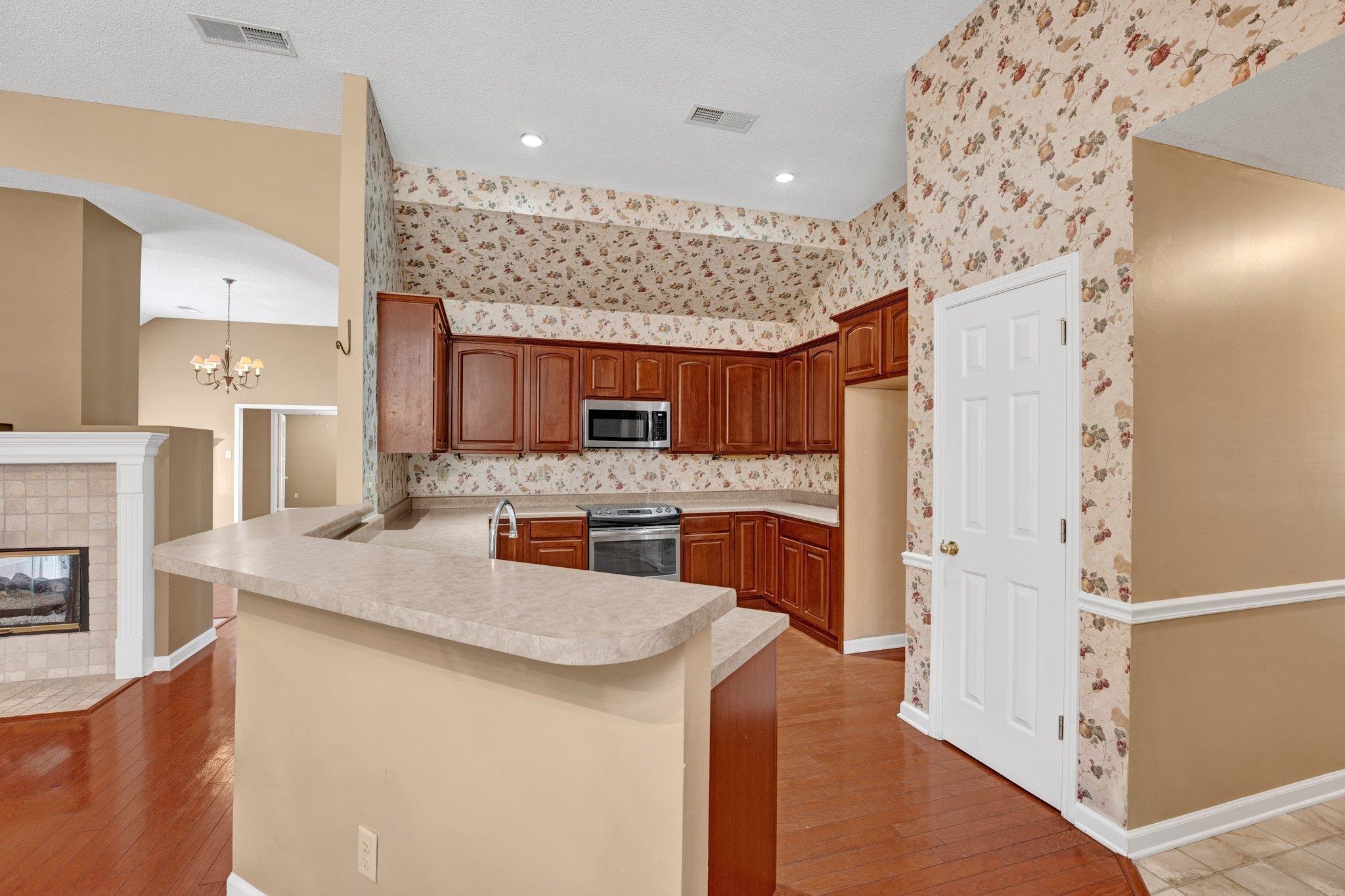 6150 Ricks Road Arlington, TN 38002 - Photo 19 of 40 Kitchen featuring an inviting chandelier, hardwood / wood-style flooring, appliances with stainless steel finishes, kitchen peninsula, and a tiled fireplace