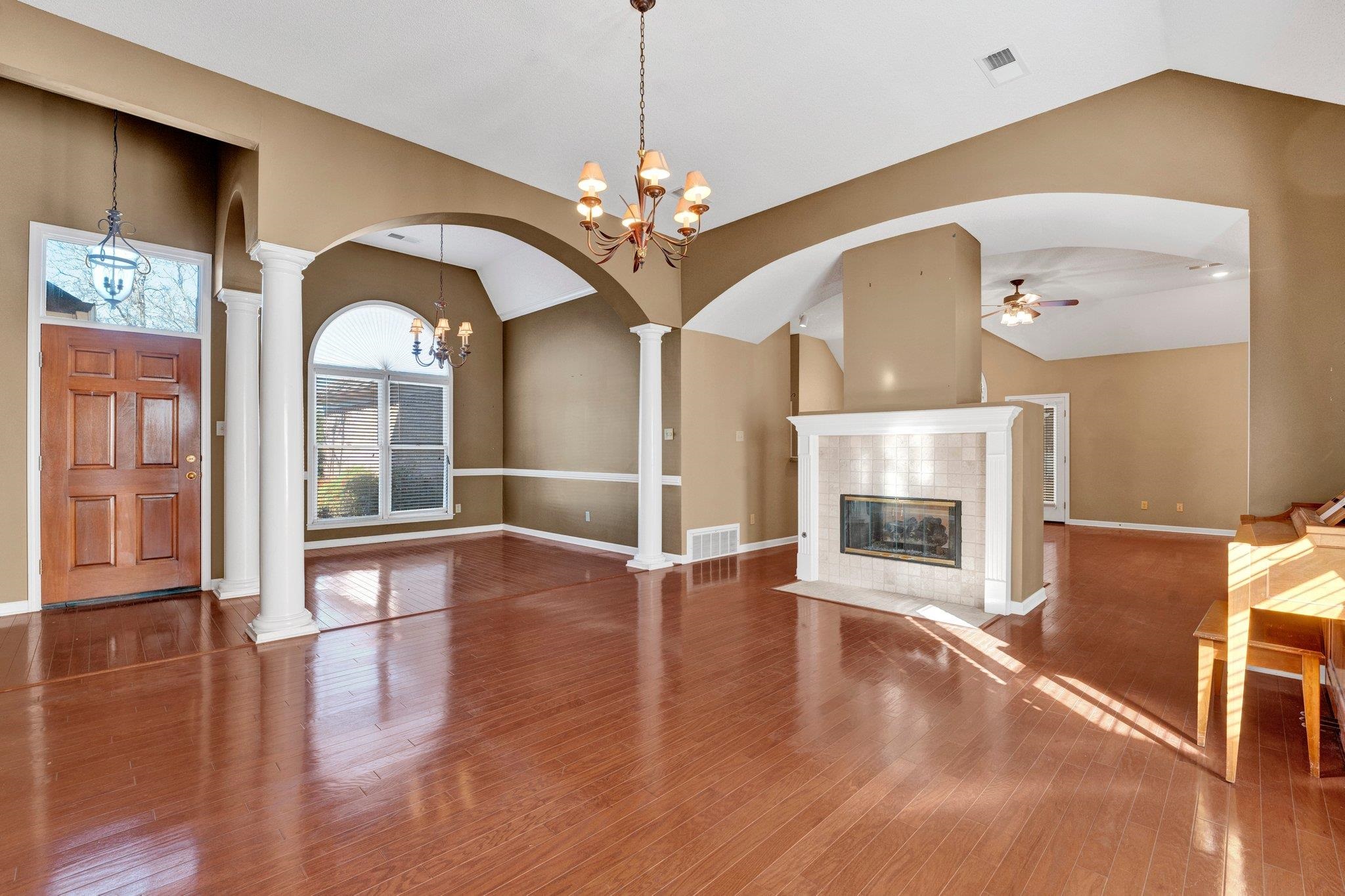 6150 Ricks Road Arlington, TN 38002 - Photo 26 of 40 Unfurnished living room with ornate columns, wood-type flooring, lofted ceiling, a tiled fireplace, and ceiling fan with notable chandelier