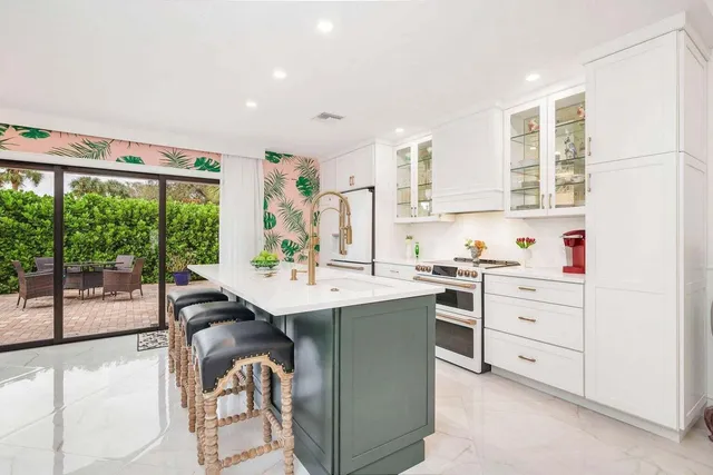 a kitchen with a stove a sink and white cabinets with wooden floor next to windows