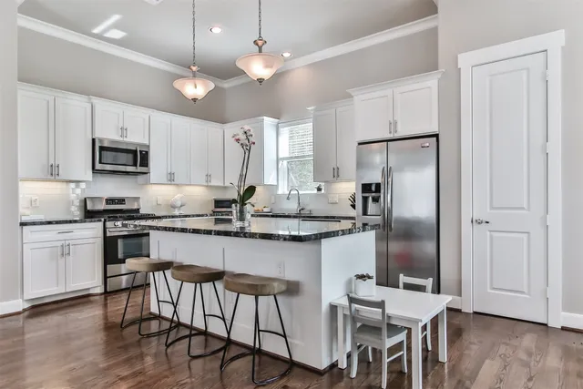 a kitchen with stainless steel appliances granite countertop a refrigerator a stove a sink a dining table and chairs with wooden floor