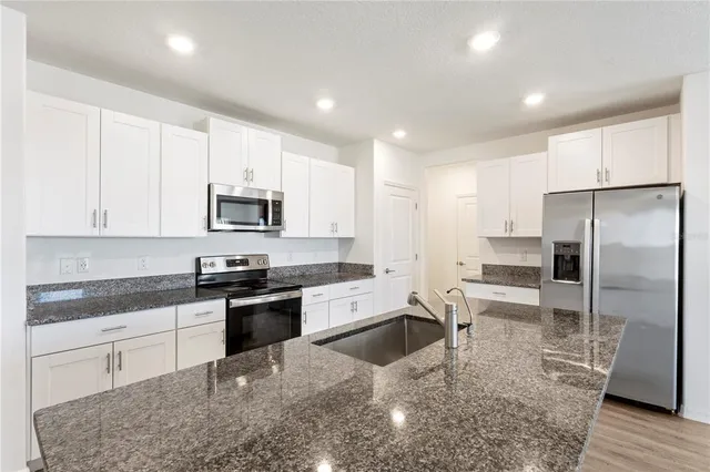 a kitchen with granite countertop a refrigerator a sink a stove a microwave and island