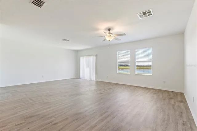 an empty room with wooden floor chandelier fan and windows