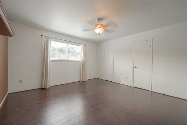 an empty room with wooden floor chandelier fan and windows