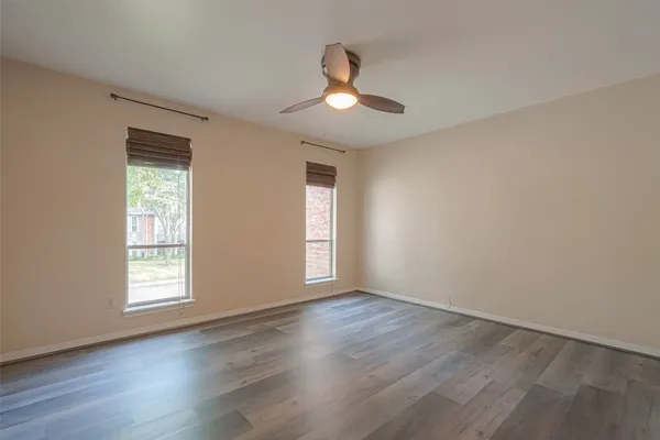 an empty room with wooden floor chandelier fan and windows