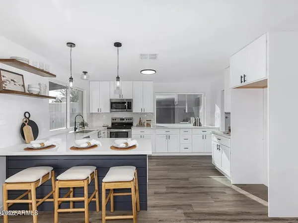 a large kitchen with granite countertop a white stove top oven a sink dishwasher and white cabinets with wooden floor