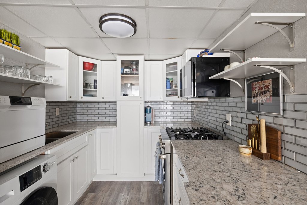 1800 Lavaca Street, Unit 207 Austin, TX 78701 - Photo 13 of 24 Kitchen with open shelves, washer / dryer, stainless steel gas stove, light stone countertops, and a drop ceiling