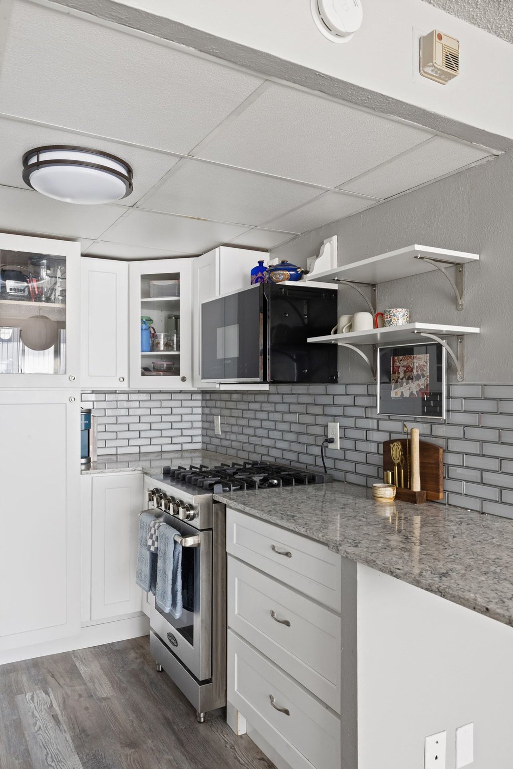1800 Lavaca Street, Unit 207 Austin, TX 78701 - Photo 15 of 24 Kitchen with stainless steel range with gas cooktop, light stone countertops, white cabinetry, black microwave, and dark wood-style floors