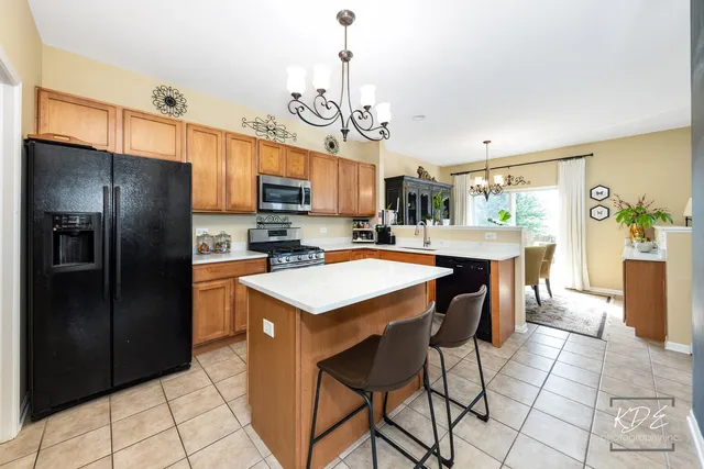 a kitchen with stainless steel appliances granite countertop a refrigerator a sink dishwasher a stove and a dining table with wooden floor