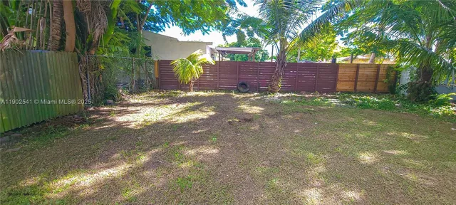 a view of a yard with large trees and wooden fence