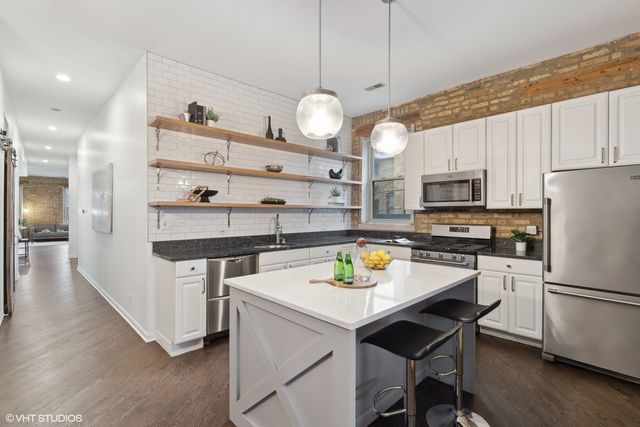 a kitchen with stainless steel appliances a stove a refrigerator and a dining table with wooden floor