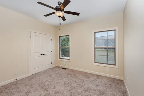 an empty room with chandelier fan and windows
