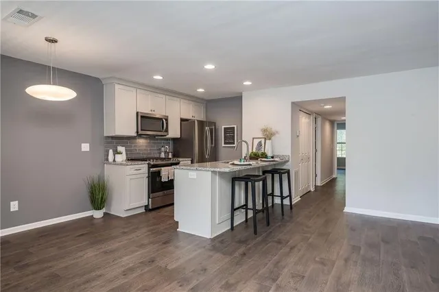 a kitchen with kitchen island granite countertop a stove top oven a sink dishwasher a refrigerator and white cabinets with wooden floor